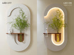 A wall-mounted decorative shelving unit shown in two states: LED OFF on the left with a white outer shell and no internal light, and LED ON on the right with the same shell illuminated from within in warm white. The unit has an organic curved shape, a wooden shelf, a glass vase with green branches, and a small white rabbit figurine.