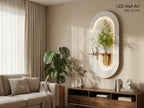 An oval LED wall art piece mounted on a beige wall in a modern living room setting. The wall art features a white outer frame with a warm white illuminated interior and a small shelf holding a green plant in a metallic pot.