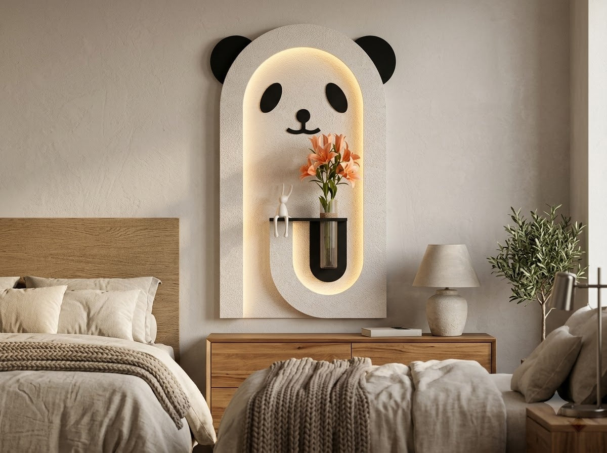 A modern wall-mounted panda-face light fixture in a bedroom setting, featuring a white arched frame with black panda ears, eyes, and nose, and warm LED backlighting. A small vase with orange flowers is mounted in the center of the fixture.